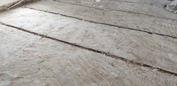 Skadad och ojämn betongplatta i ett renoveringsprojekt med synliga sprickor och skräp.