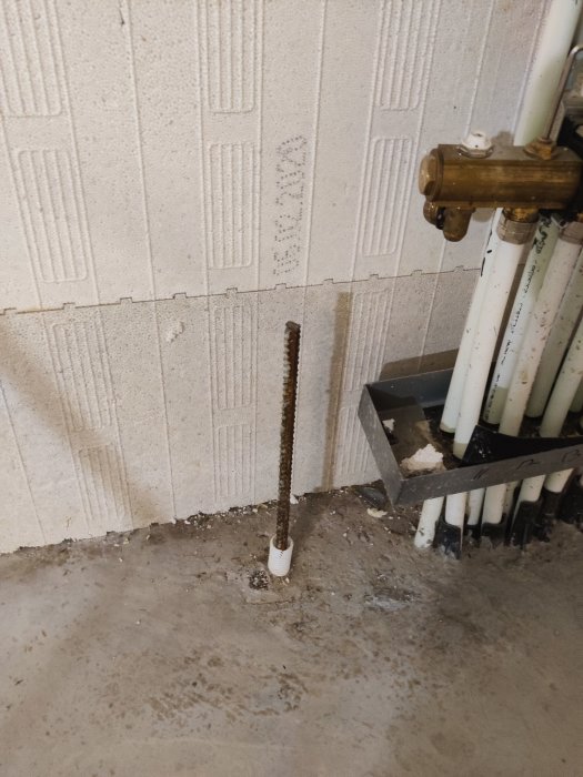 Armeringsjärn fastgjutet i betong vid golvvärmerör och vattenledningar i ett byggprojekt.
