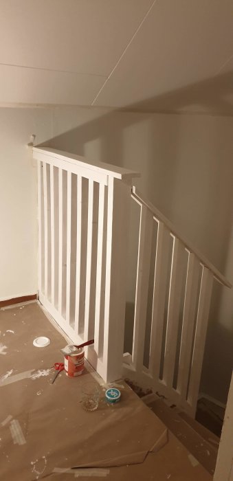 Renoverad trappa med nymålat, vitt räcke och arbetsmaterial synligt på golvet.