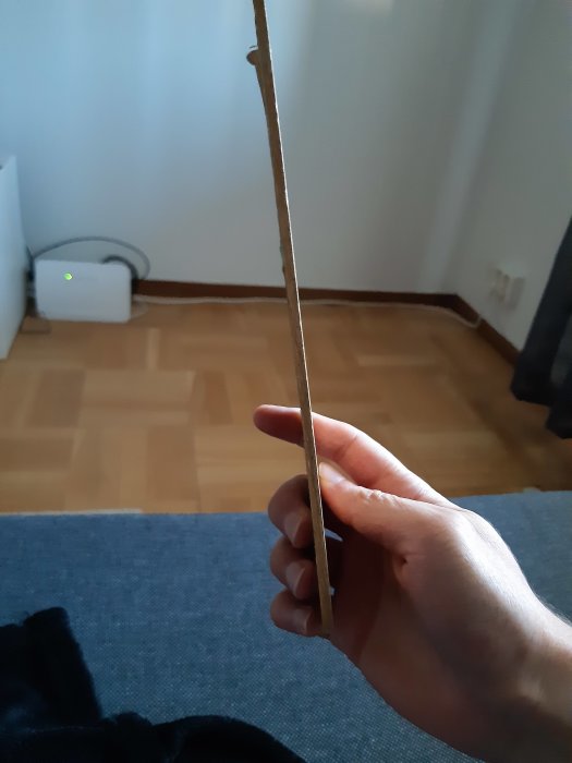 Hand håller ett skadat parkettgolvstycke framför ett golv med liknande mönster.