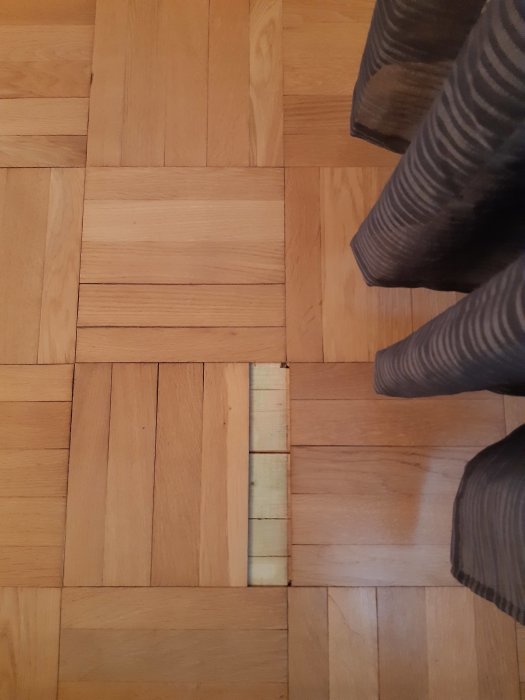 Parkettgolv med vissa skadade vattenfläckade rutor nära möbelben.