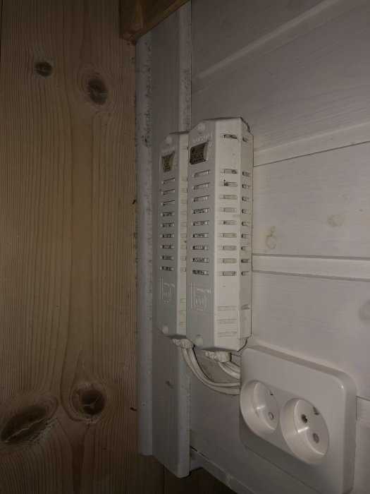 En gammal vit säkringslåda bredvid ett vägguttag på en trävägg.