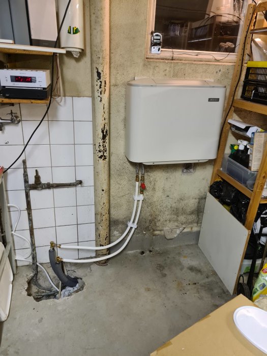 En värmepump installerad i ett källarrum med synliga rör och kablar runtomkring.