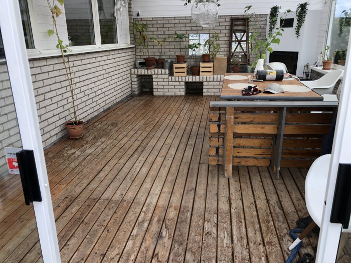 Uterum med trägolv, vit tegelvägg, möbler och krukväxter före golvvärmeinstallation.