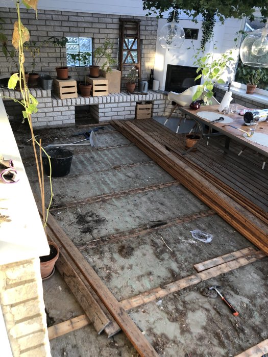 Rivet golv i ett uterum under renovering med verktyg och avlägsnat material synligt, visar betongplattan och jord.