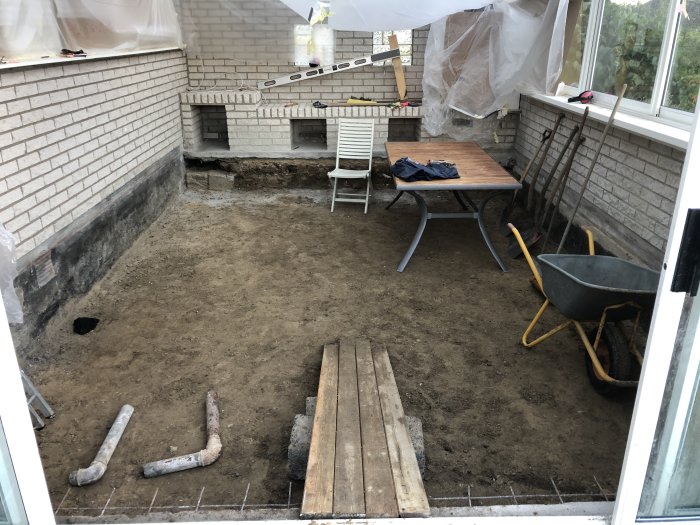 Uterum under renovering med borttagen betongplatta, grävverktyg och skottkärra.