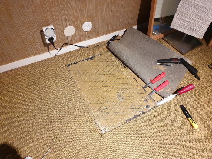 Golv med uppvikt matta avslöjar betongplatta och verktyg för inspektion av avlopp och isolering.