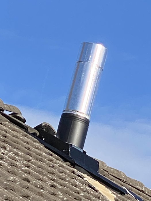 Isoleringsrör för Contura kamin som sticker upp genom ett tak täckt med takpannor mot en klarblå himmel.