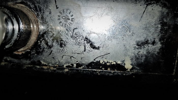 En sliten metallplatta med text och siffror, nära en röranslutning i ett badrum.