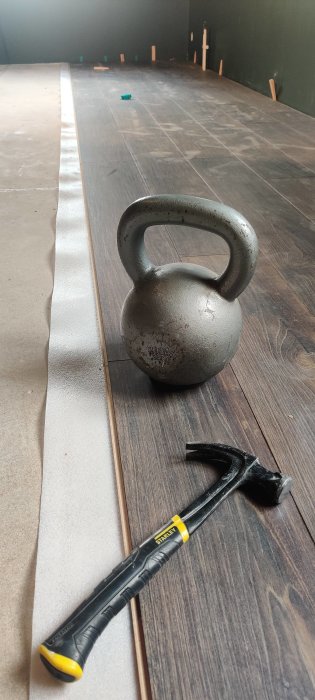 Kettlebell och hammare framför nyinstallerat mörkt laminatgolv under renovering.