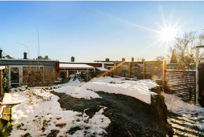 Trädgårdstomt med stora stenar och snötäckta områden, omgärdad av trädgårdar och radhus.