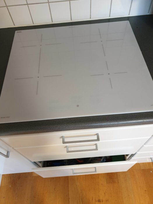 Induktionshäll installerad i kök ovanpå vita lådor, med en säkring avstängd för en oanvänd fas.