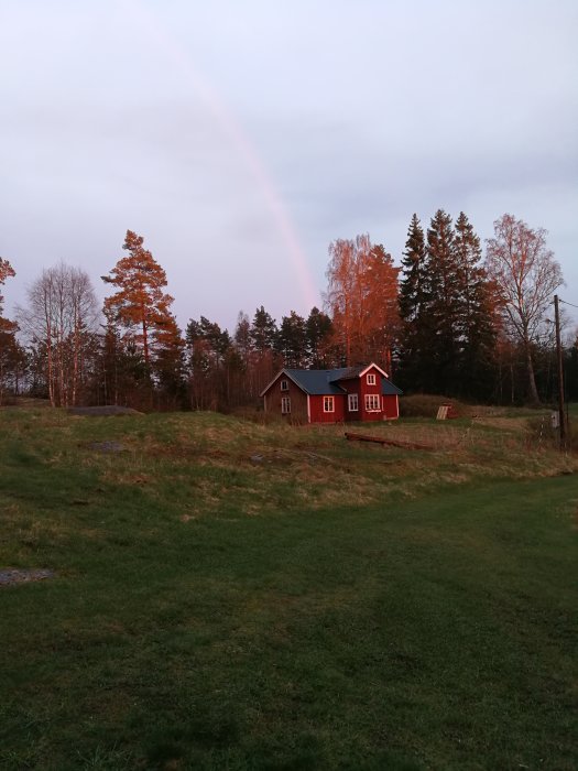 Rött äldre hus utan omgivande byggnader på en tomt, regnbåge i skymningen över huset.