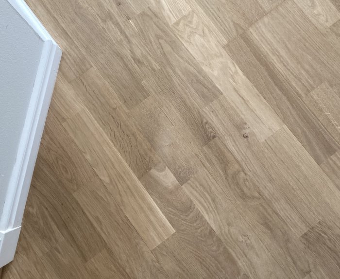 Ljus parkettgolv med små springor och färgvariationer, närbild med synlig dörrtröskel.