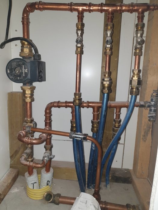 Värmesystem med kopparledningar, cirkulationspump och blandventil i ett garage.