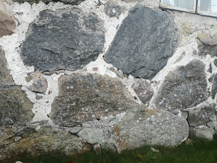 Väggparti av en gammal byggnad med natursten och slitet vitaktigt kalkbruk mellan stenarna.