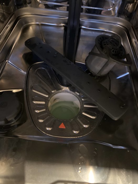 Diskmaskinsdelar placerade oorganiserat i en diskmaskin efter rengöring, inklusive ett spolarm och filter.
