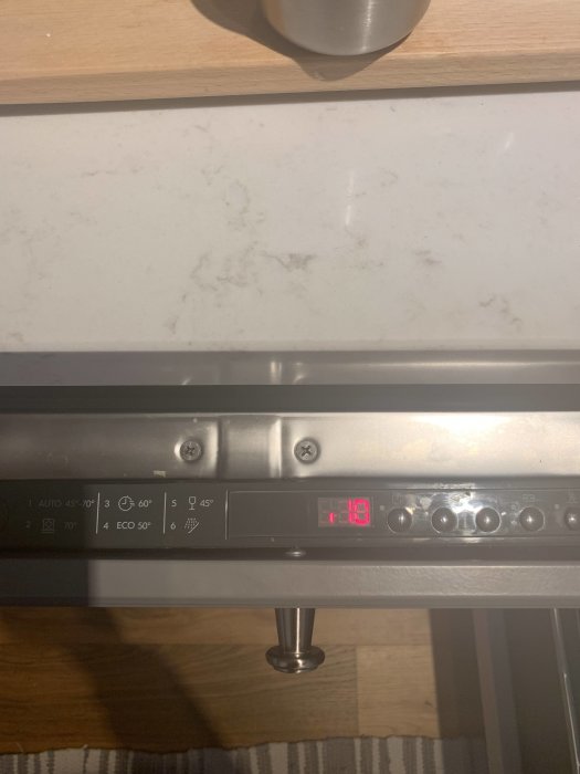 Digital display på diskmaskin som visar återstående tid, omgiven av kontrollknappar och köksinredning.