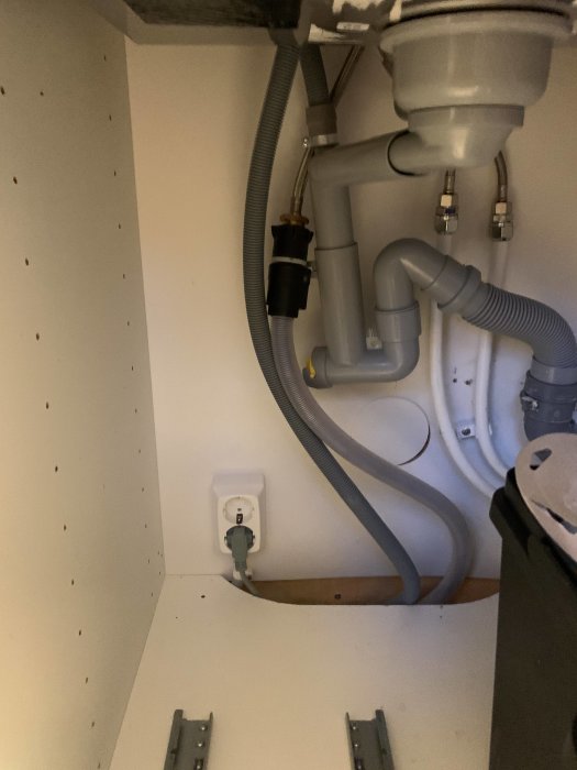 Vattenlås och rör under köksskåp med synlig strömbrytare och kopparledningar, möjlig frågeställning om vattenventil.