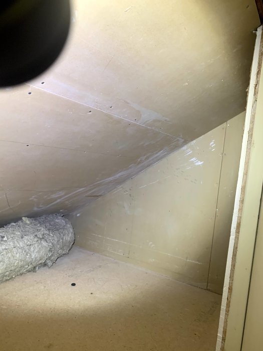 Vy genom glipa på en vind med isolering och spånskivor, där högra delen ser lite kletig ut.