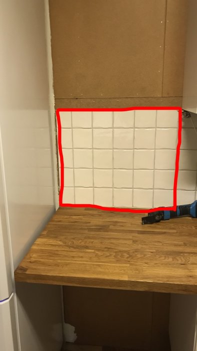 Köksvägg under renovering med borttagna skåpstommar och markerat kakelområde för kapning.