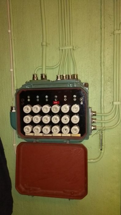 Elektrisk fördelningslåda med öppen röd lucka och flera anslutna kablar på en grön vägg.