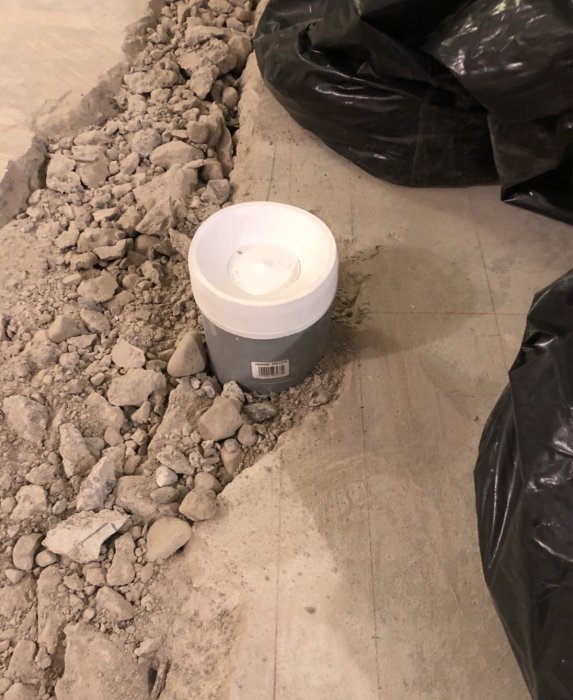 Grus och gammal betong på betonggolv där avloppsstammar byts, grå avloppsrör synligt.