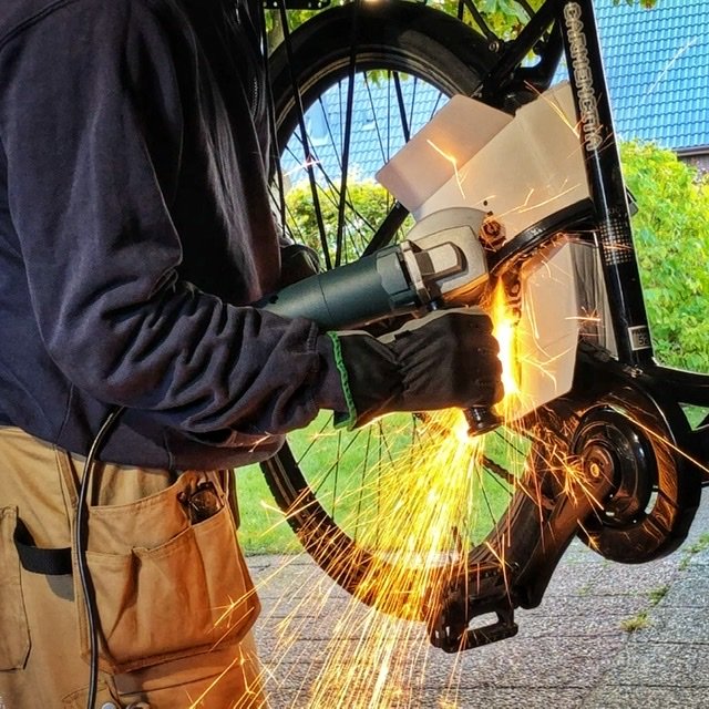 Person använder en vinkelslip för att arbeta på en cykels komponent med gnistor som flyger.