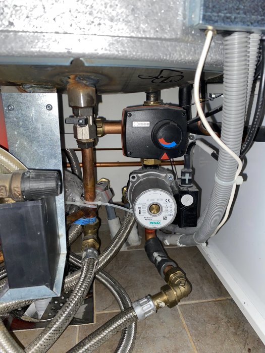 Värmepump och golvvärmesystem med synliga rör och reglage under installation.