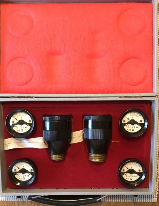 Tre gamla svarta eluttag och två manometermätare i en röd fodrad låda.