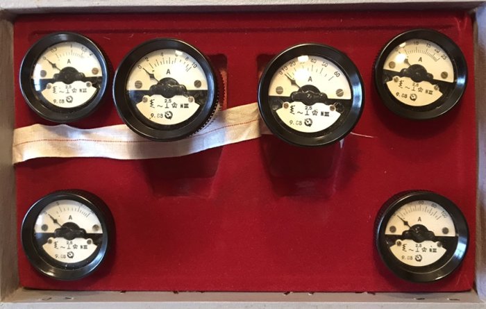 Gammaldags amperemätare i låda, förvarade med ett vitt band genom mitten.