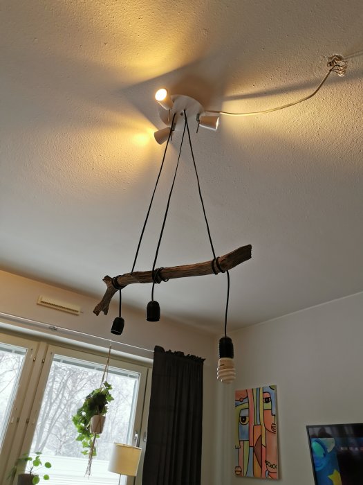 Taklampa med gren och tre hängande lampor, en tänd lampa speglar ojämnt ljus.