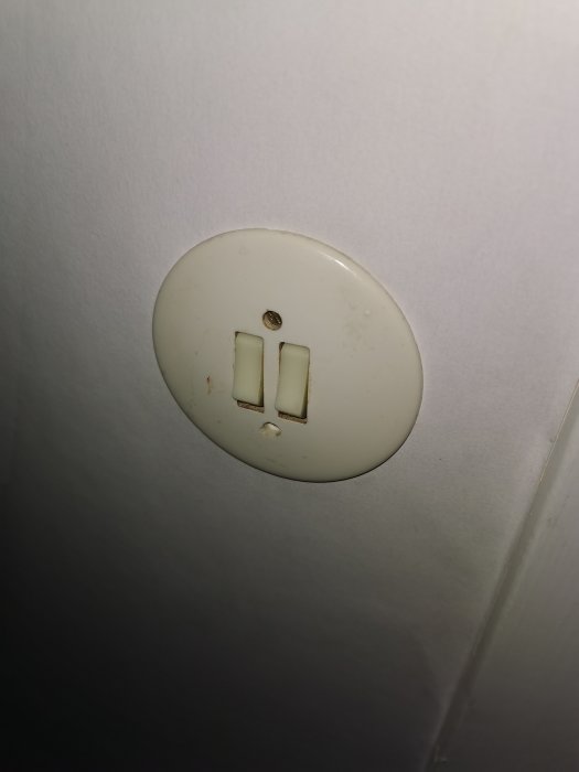 En gammal vit dubbelströmbrytare på en vägg, vilket indikerar en installation utan jordledning.