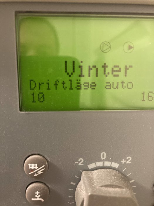 Display på värmepump med texten "Vinter" och "Driftläge auto", omgivet av knappar och inställningsreglage.