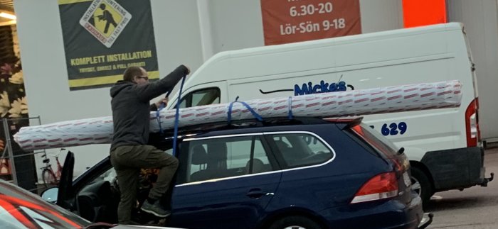 Person fäster en ny matta på takräcket av en bil utan skydd för lacken.