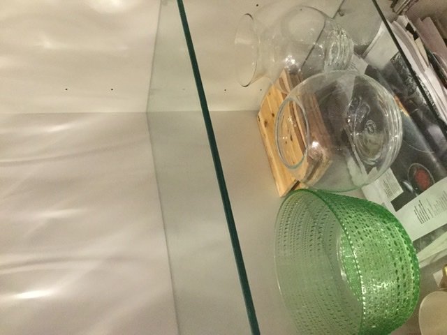Transparenta glashyllor med olika tonade kanter, delvis täckta av glasföremål.