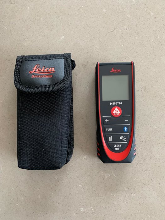 Leica Disto 2 lasermätare bredvid dess väska på grått underlag.