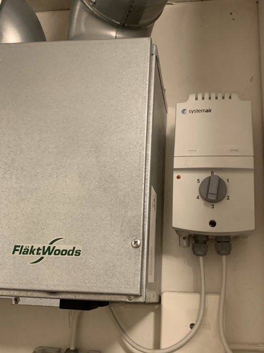 Ventilationsenhet från FläktWoods och anslutet Systemair reglage på en vägg.