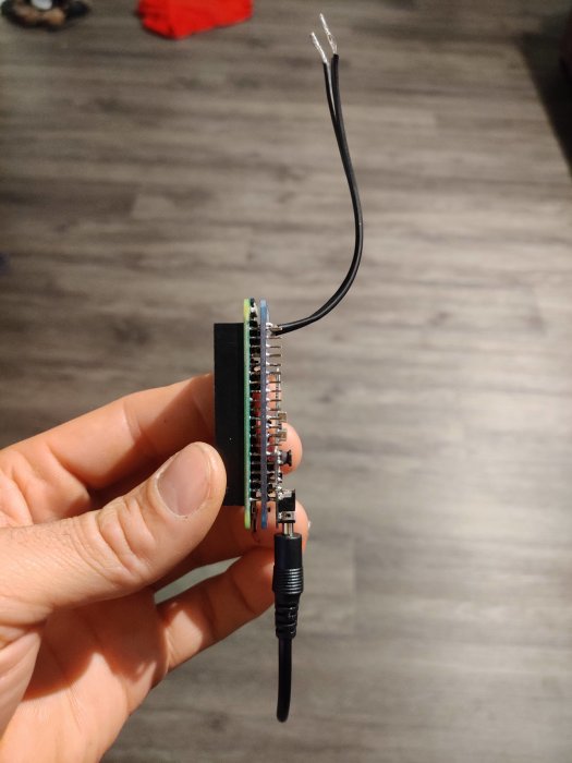 En hand håller en Raspberry Pi kretskort ansluten till en svart kabel, tänkt att monteras i en värmepump.