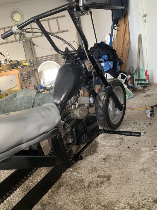 Svart trimmad moped under konstruktion i ett rörigt garage.