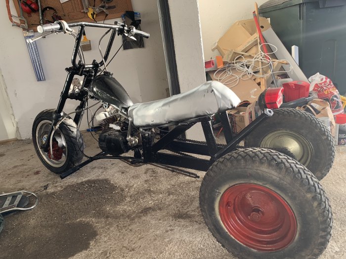 Egenbyggd trehjulig motorcykel i ett garage med röda fälgar och stort bakhjul.