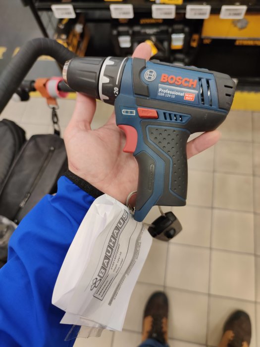 Hand håller en Bosch GSR 12v-15 skruvdragare i butik, med Bauhaus kvitto.