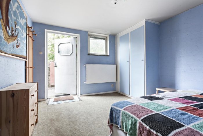 Ett inrett rum med öppen dörr ut till gatan, blåmålade väggar, en säng och inbyggda garderober.