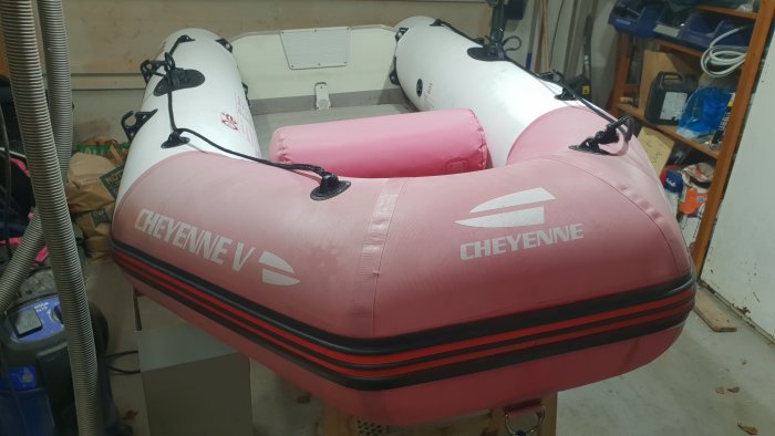 Uppblåsbar rosa och vit gummibåt med texten "CHEYENNE" i ett garage.