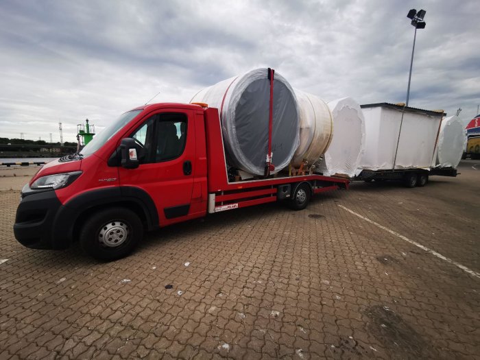 Lastbil transporterar fabriksmålade byggmoduler inplastade på flak.