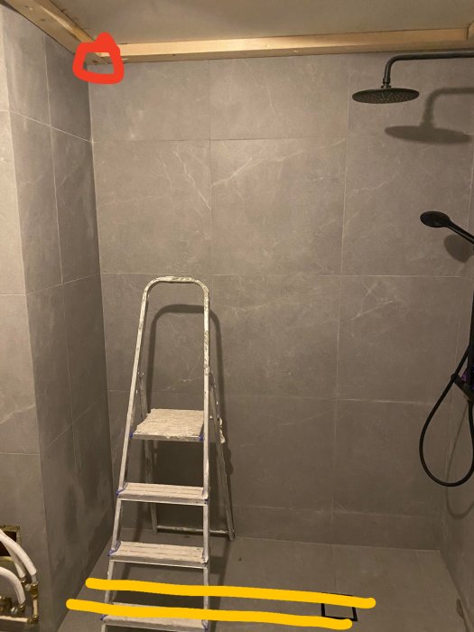 Badrum under renovering med grå kakelväggar, en stege och markerade borenheter och rörledningar.