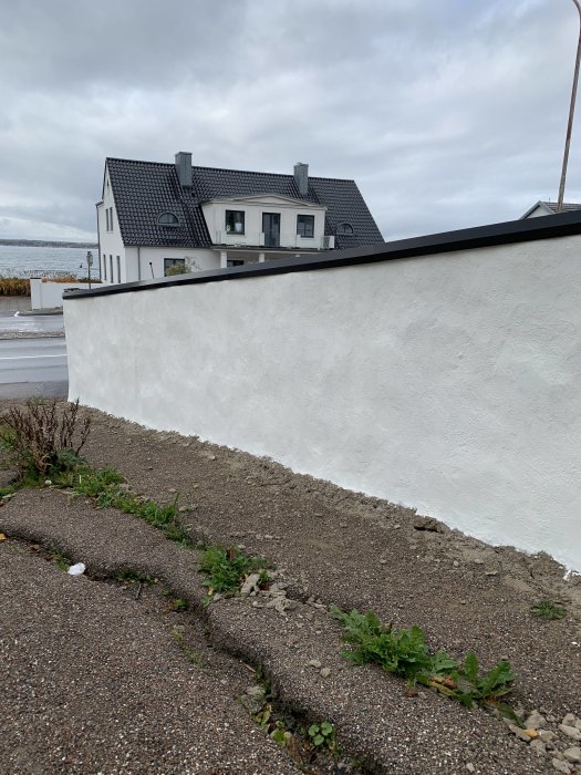 Ojämnt böjd plåt på murkanten av en vitputsad mur med bakgrund av ett hus och molnig himmel.