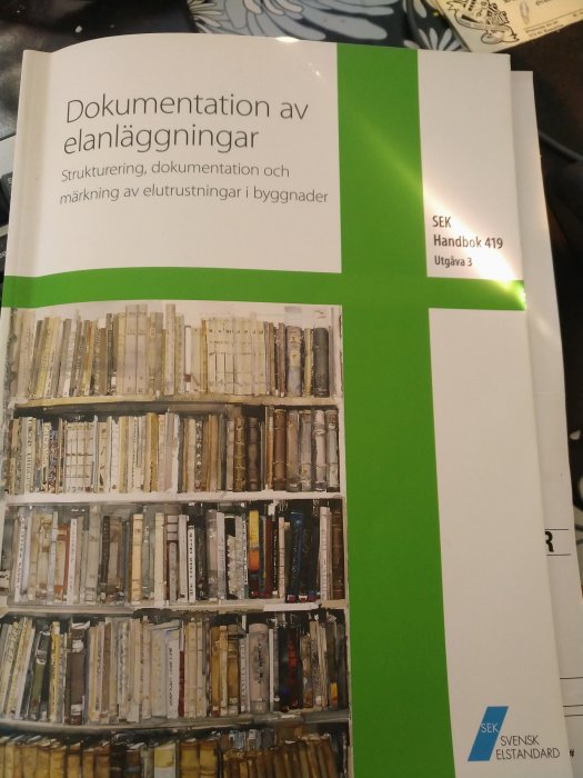 Handbok om dokumentation av elanläggningar bredvid en hylla med gamla, slitna böcker.