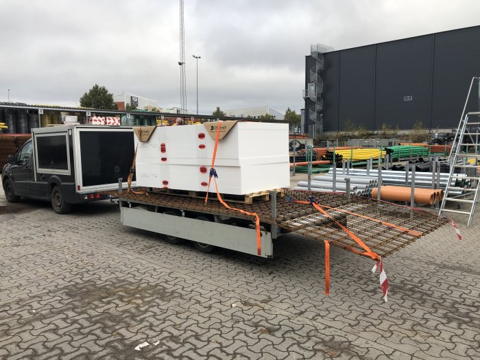 Lastbil med släp lastat med byggmaterial på en parkeringsplats.