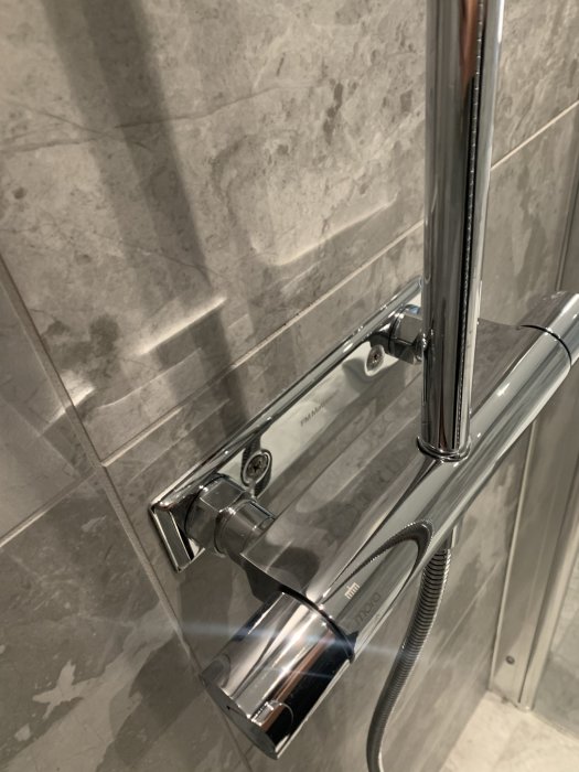 Kromad duschblandare och kontroller mot grå marmorkakelvägg.